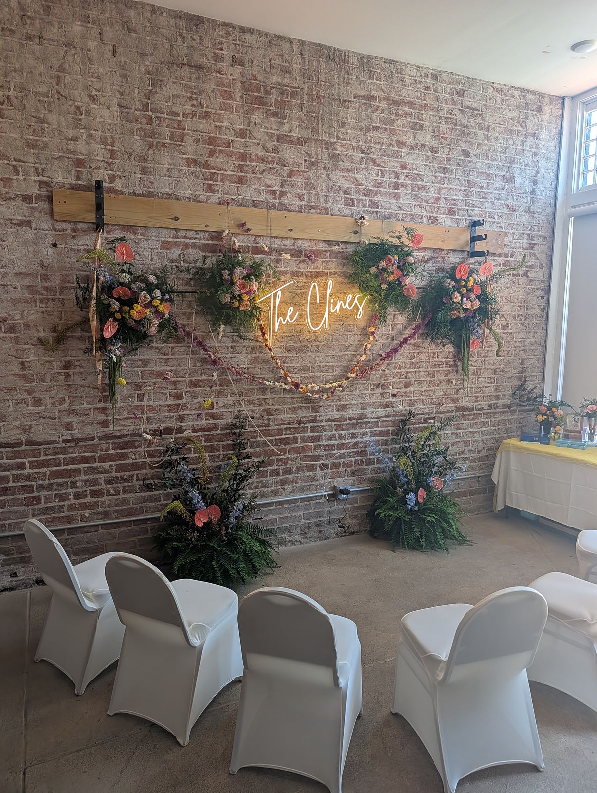 A wedding ceremony wall with florals and a neon sign